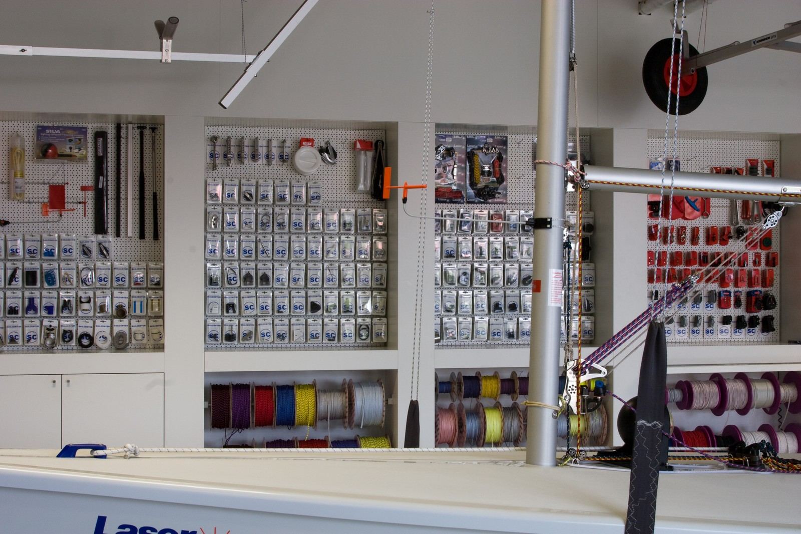 Wandkast met pegboardvakken en touwspoelen achter een zeilboot.