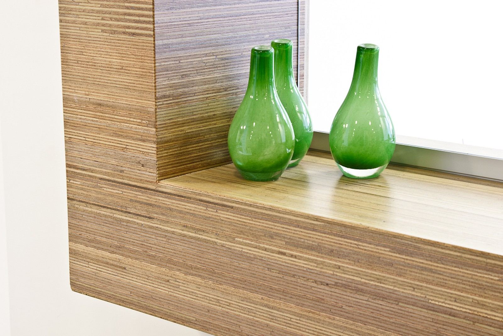 Wandplank van plexwood® meranti onder een raam, met glazen vazen.