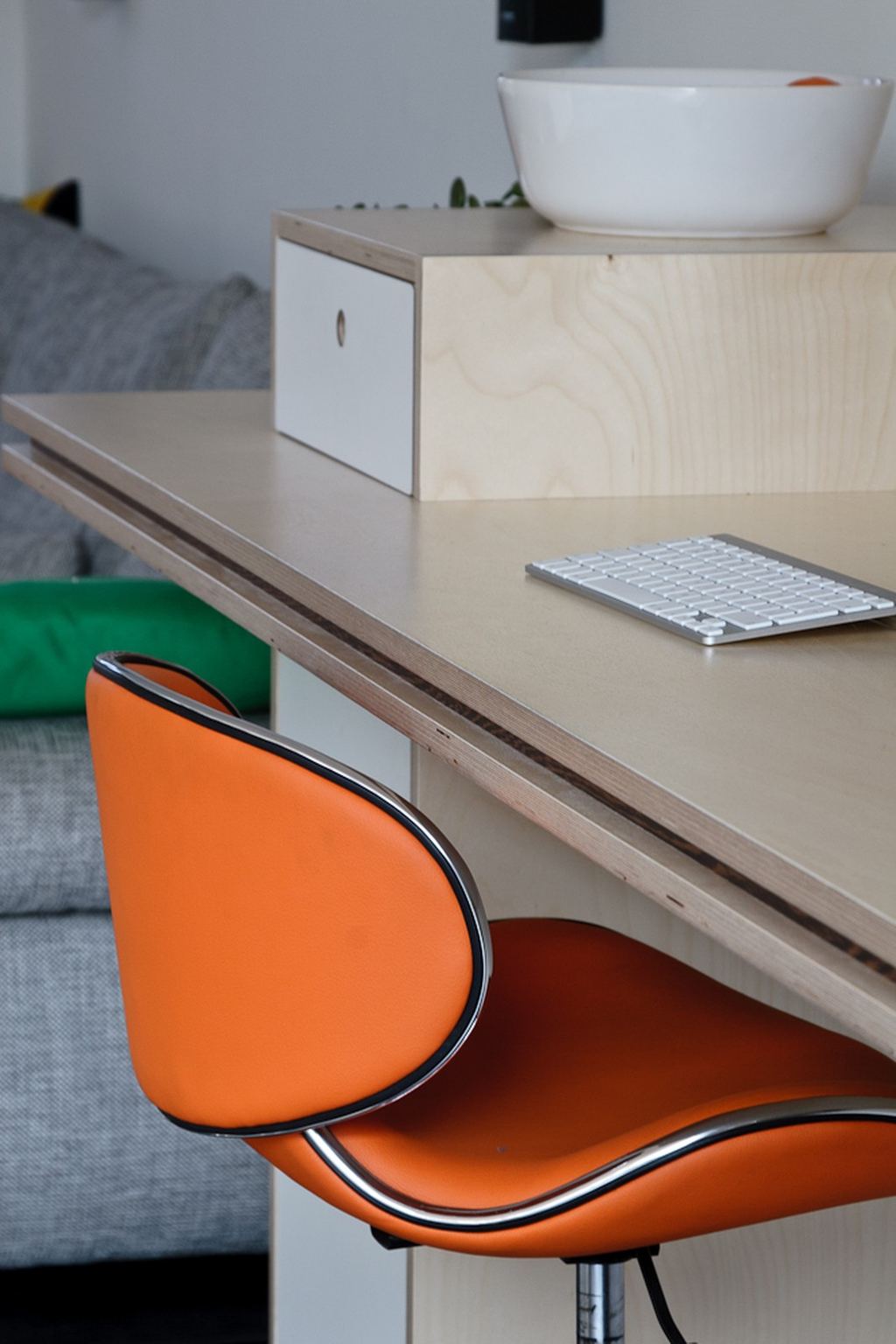 Detail van een bureau met een lichte lade met wit front, naast een oranje stoel.