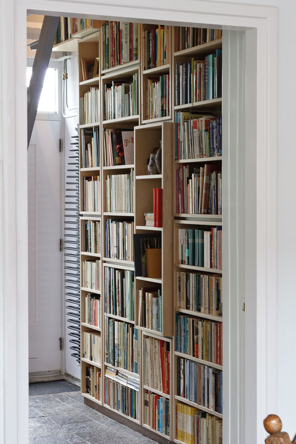 Wandvullende boekenkast van berken multiplex met een uitstekend vak in het midden.