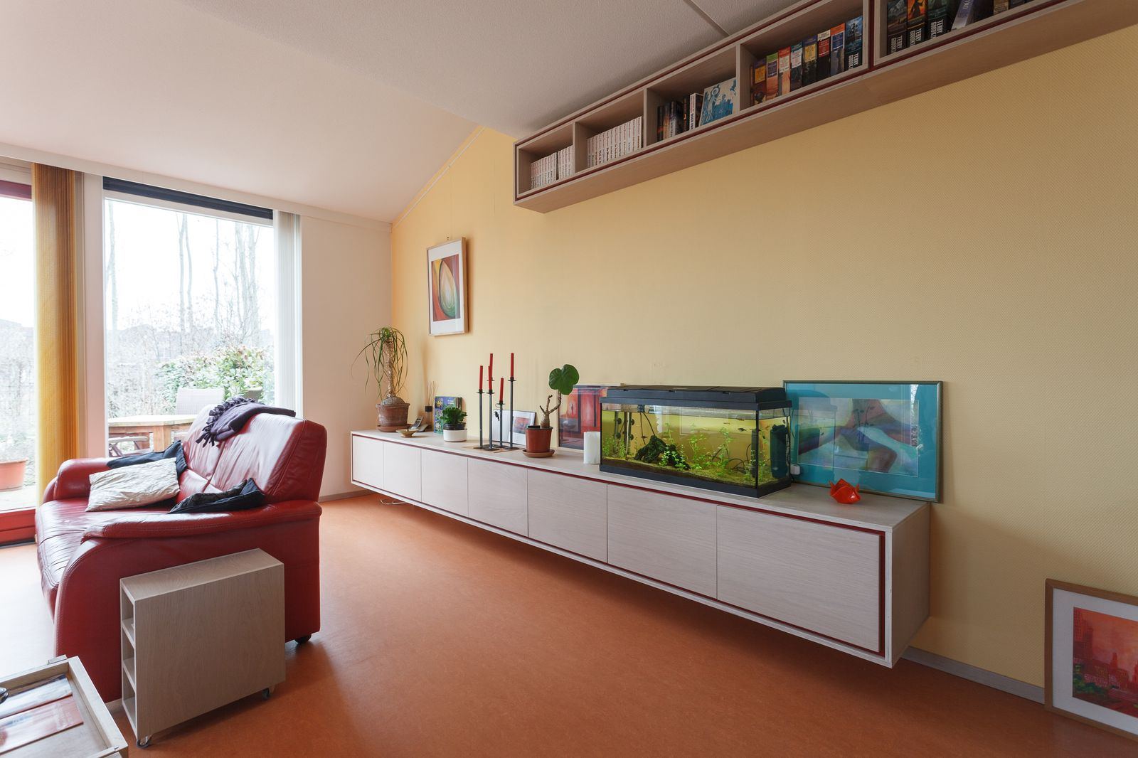 Zwevend dressoir met rode HPL-rand, onder een wandkast vol boeken.