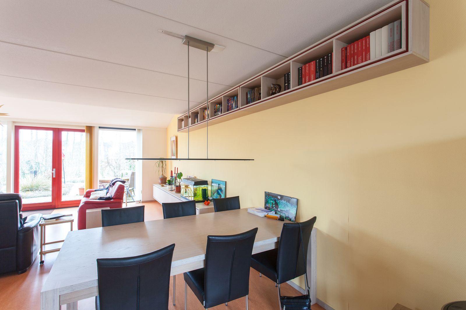 Eettafel met stalen onderstel, onder een wandkast met rode accenten.