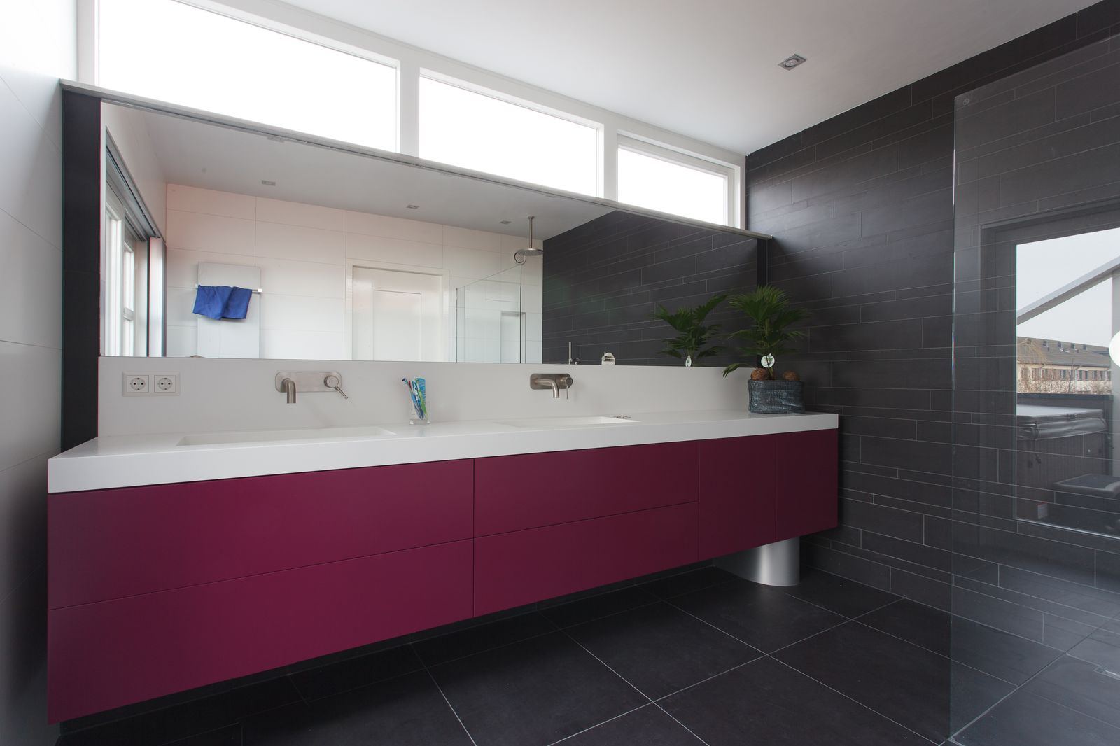 Zwevend badkamermeubel in magenta met een breed wit blad en twee wastafels.