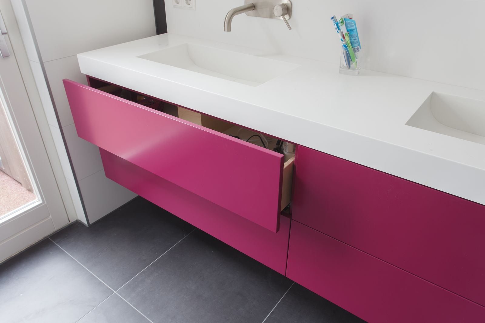 Badkamermeubel in magenta met een witte wastafel, met een lade open die een houten binnenkant toont.