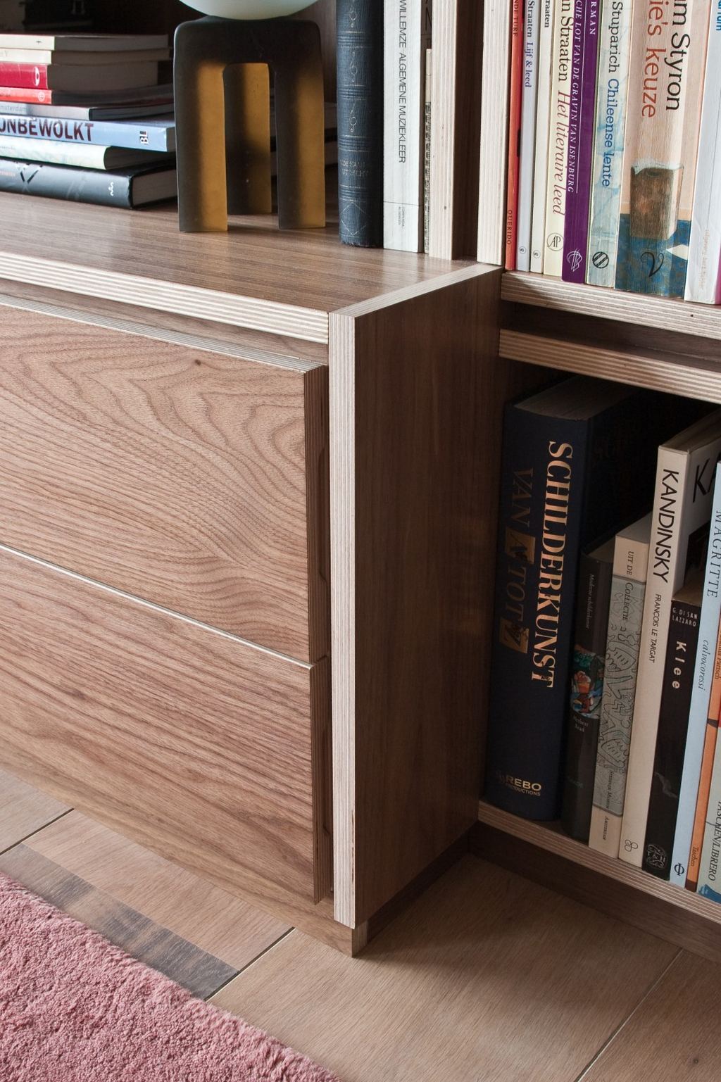 Detail van de hoek van de lage kast, met houten laden naast een vak vol kunstboeken.