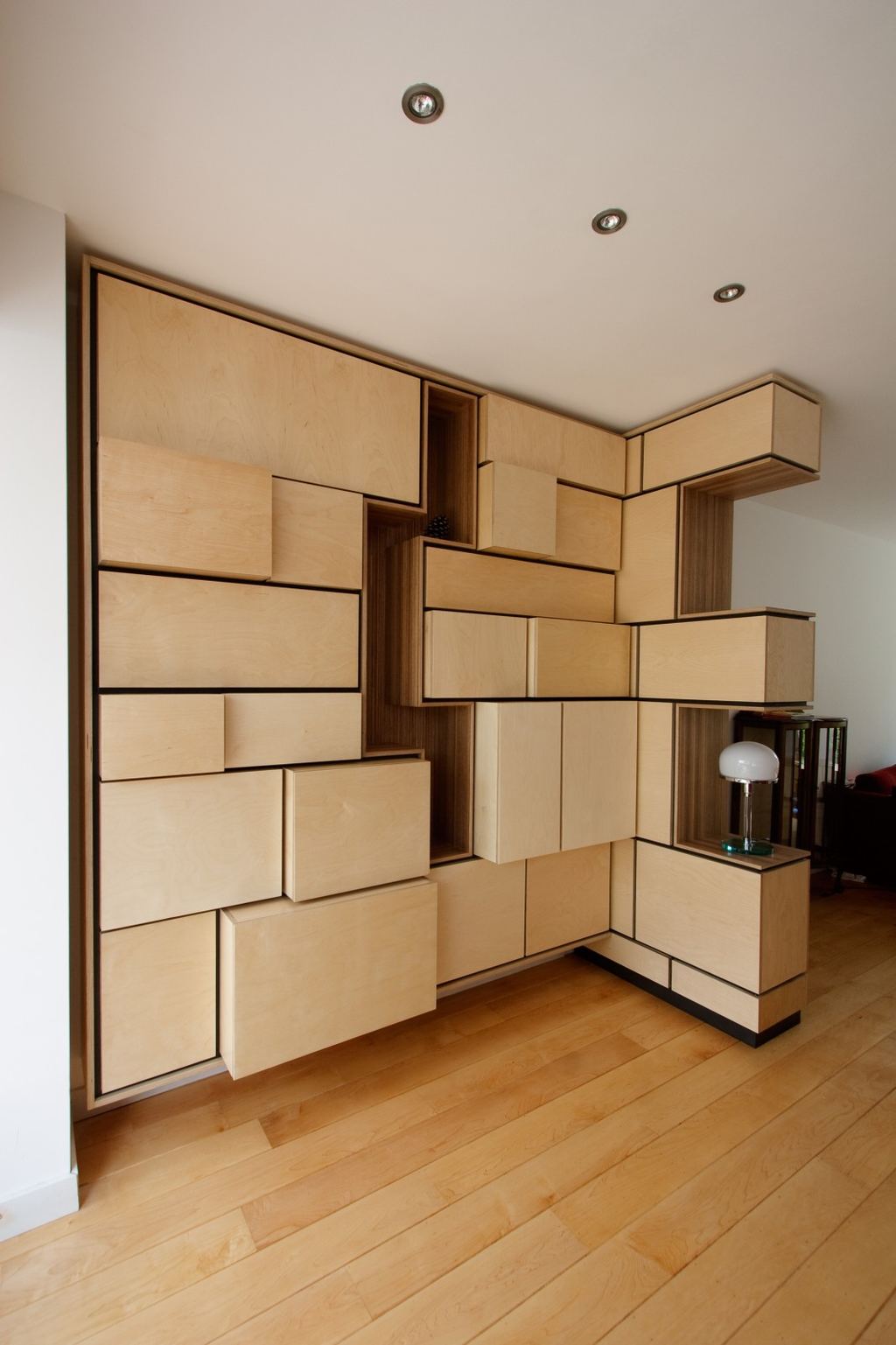 Wandkast met een onregelmatig patroon van vierkante en rechthoekige fronten in lichte houtkleur.