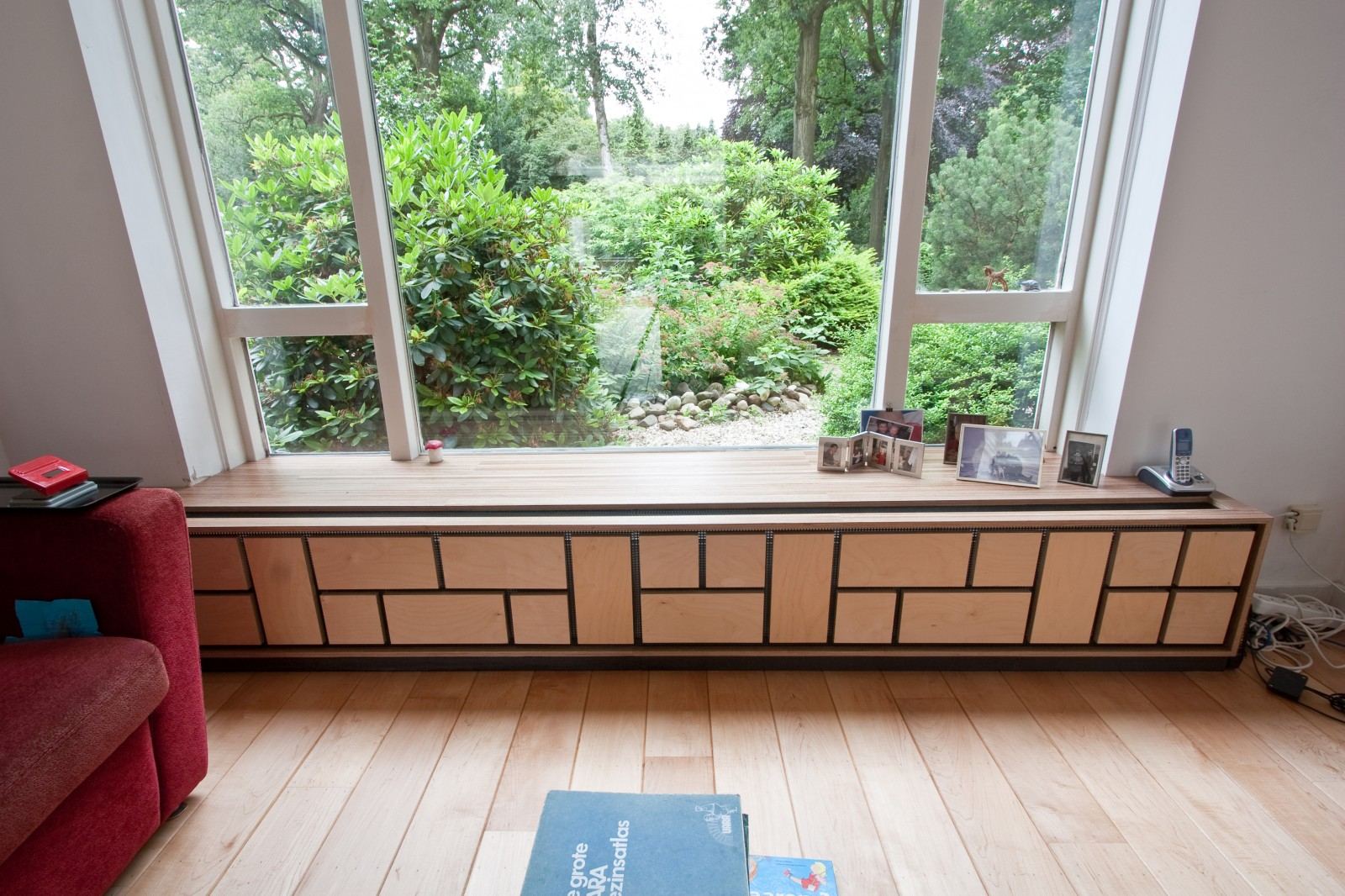 Lage bank onder een groot raam, met een patroon van kleine rechthoekige houten panelen.