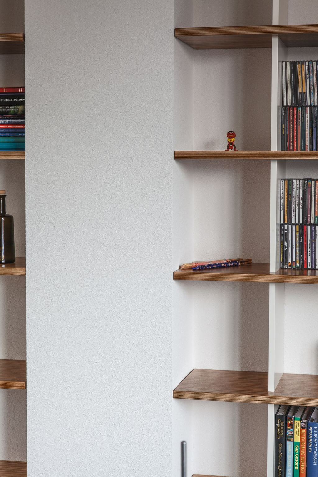Detail van open boekenplanken met cd's en een klein beeldje erop.