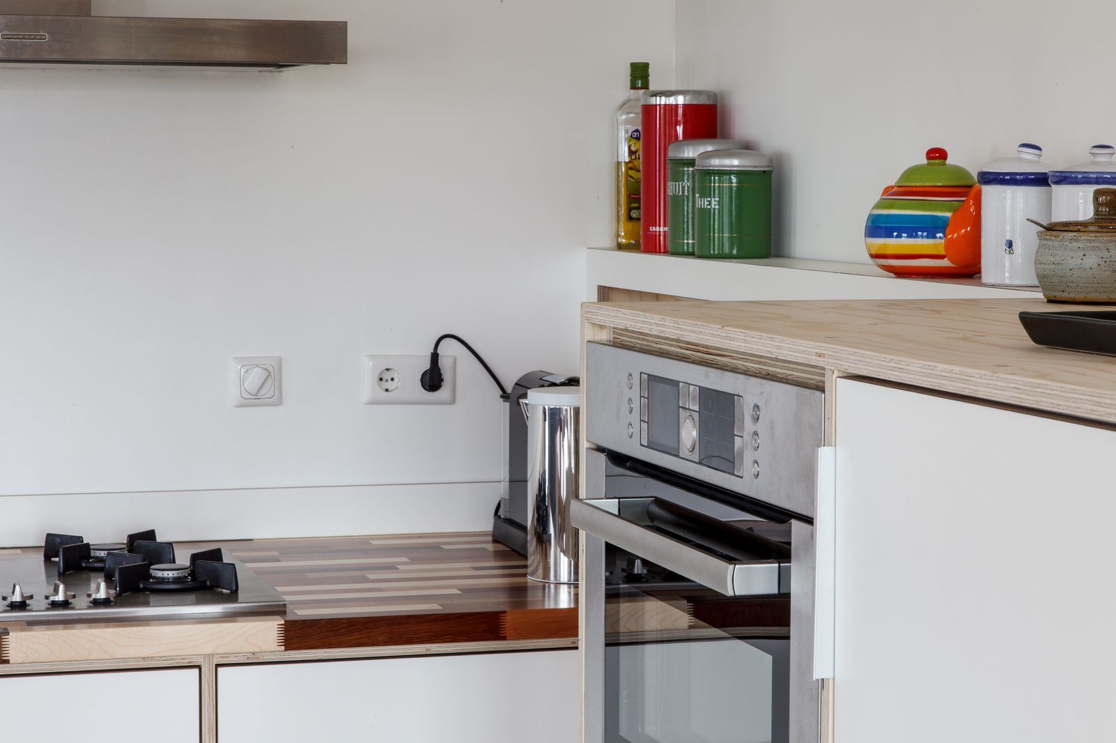 Ingebouwde oven met houten omlijsting, opengetrokken onder een plank met potten.