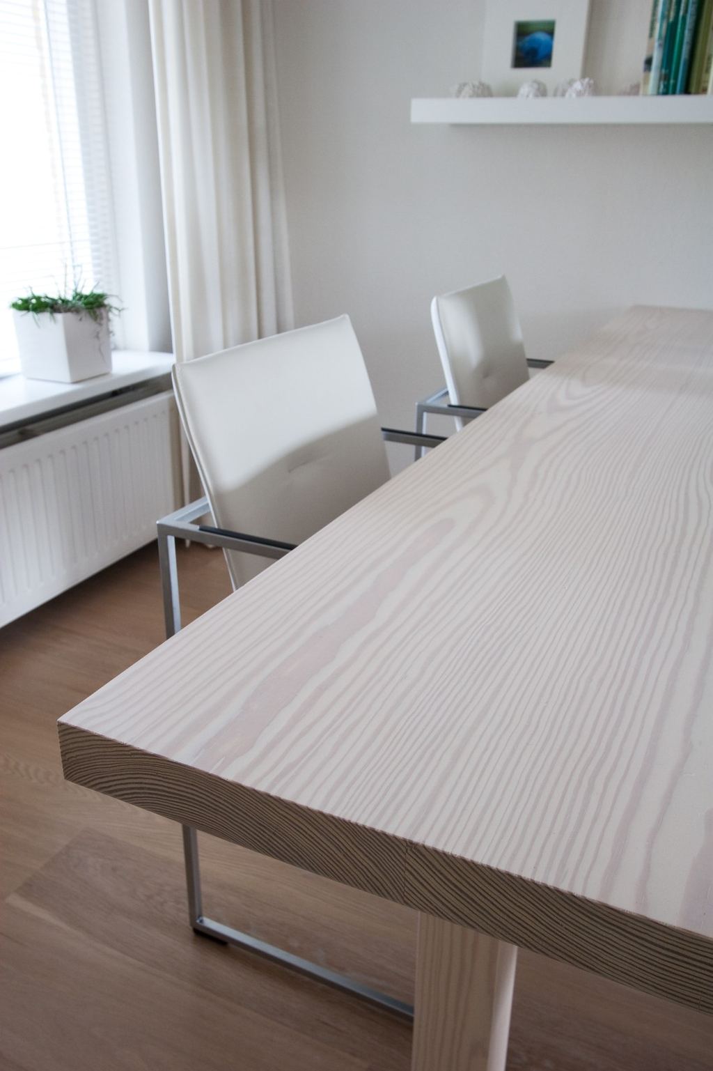 Tafel met een dik houten blad op een smal chromen onderstel, met witte stoelen ernaast.