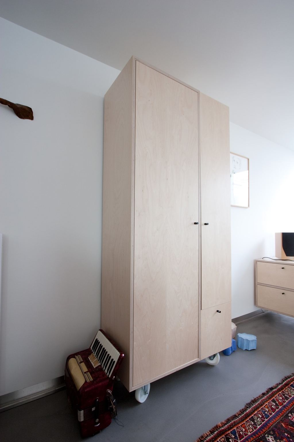 Kast van licht hout op wieltjes, met twee deuren en een lage lade.
