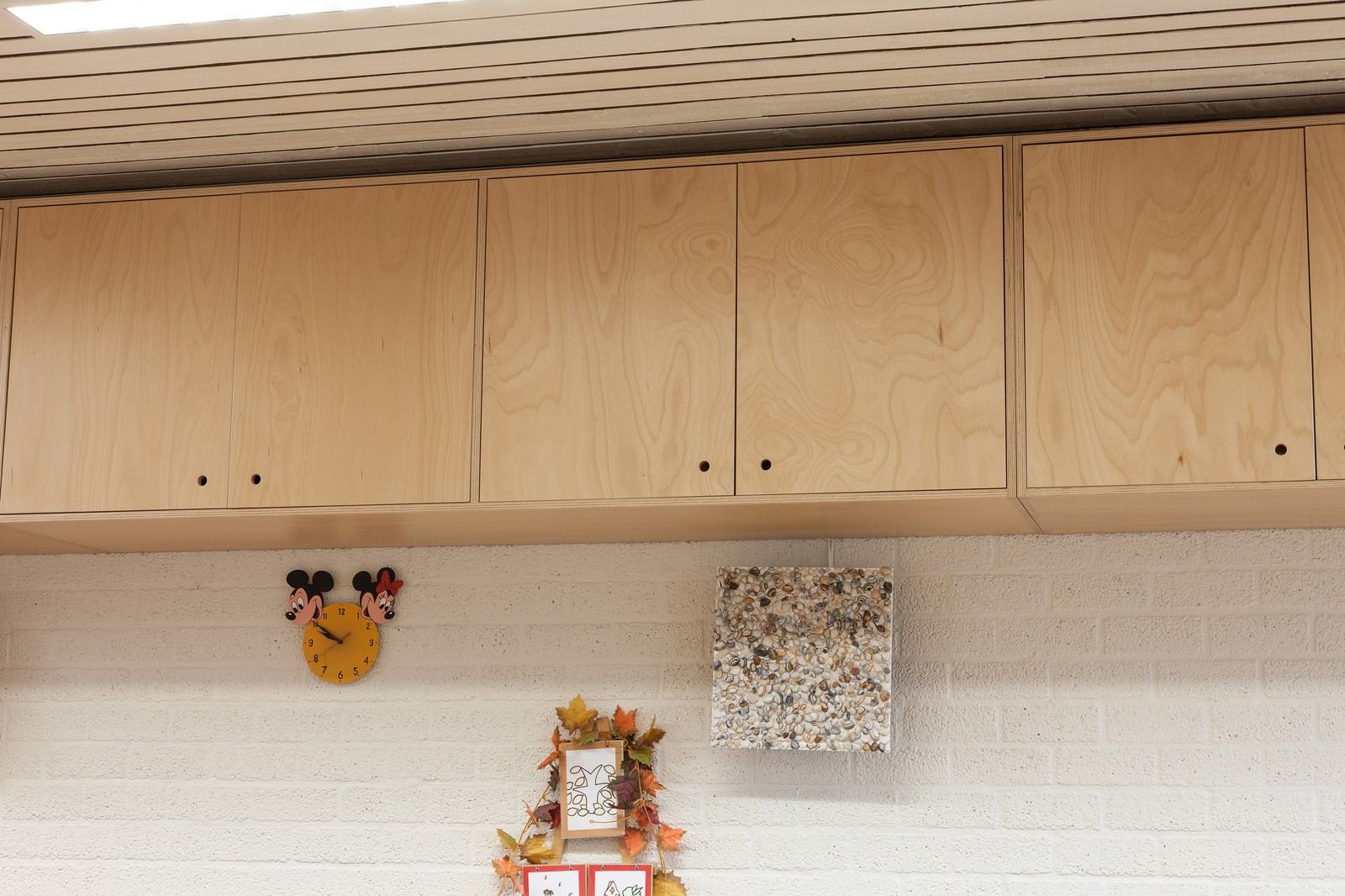 Wandkasten in berken multiplex, hoog tegen de wand gemonteerd.