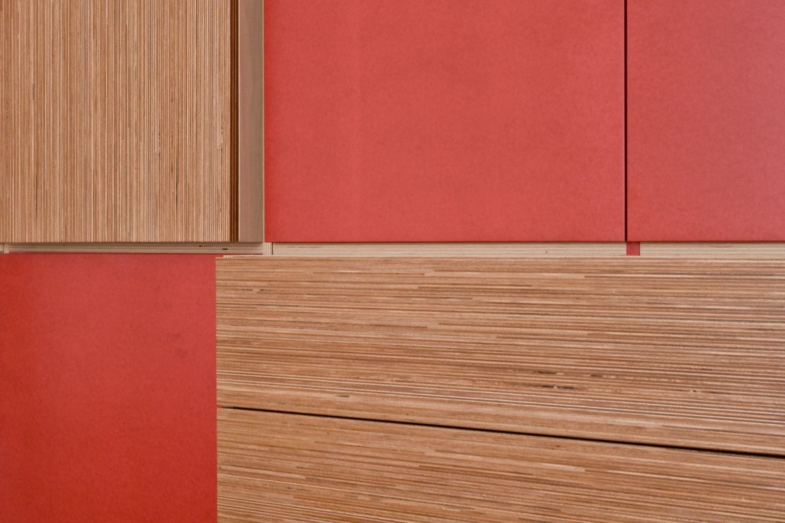 Detail van een rood paneel naast een plexwood ladenfront.