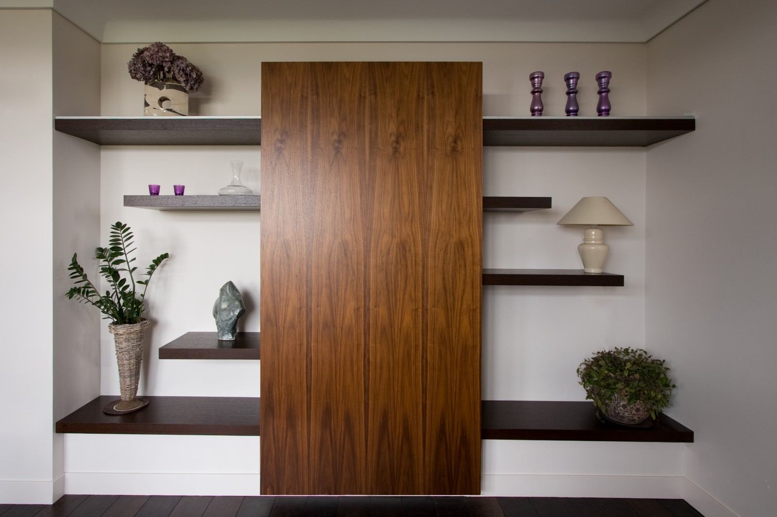 Notenhouten schuifpaneel tussen zwevende wenge planken met decoratie.
