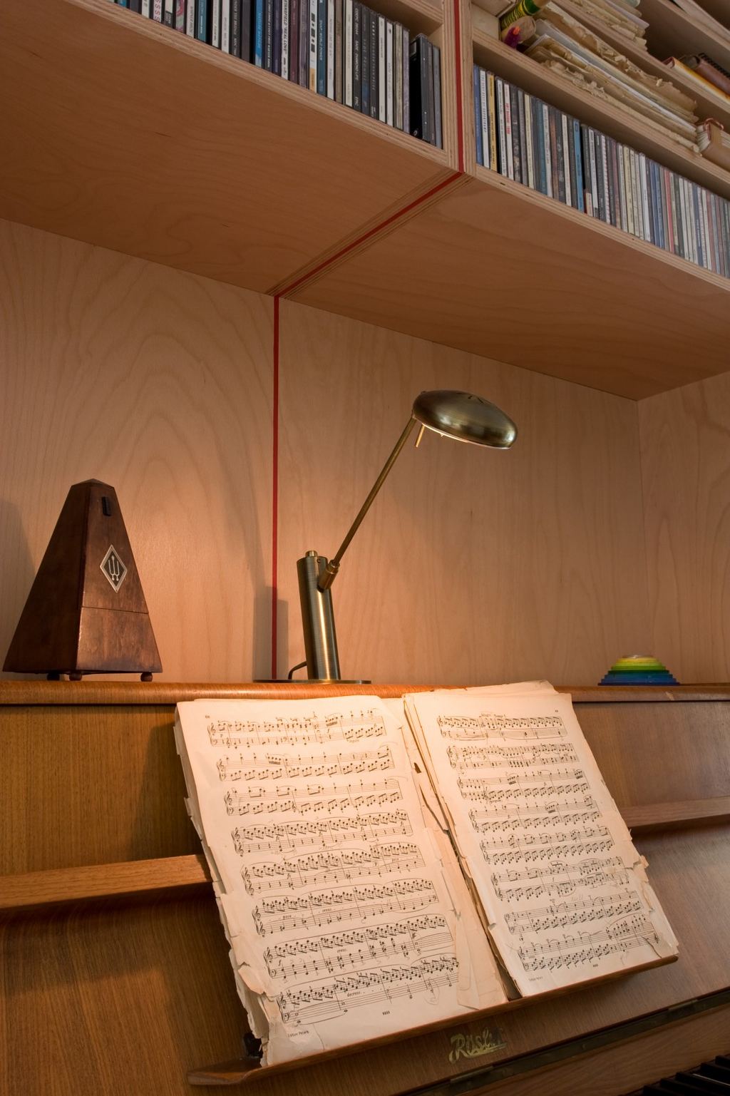 Detail van een houten planklegger met een metronoom en een lamp erop.