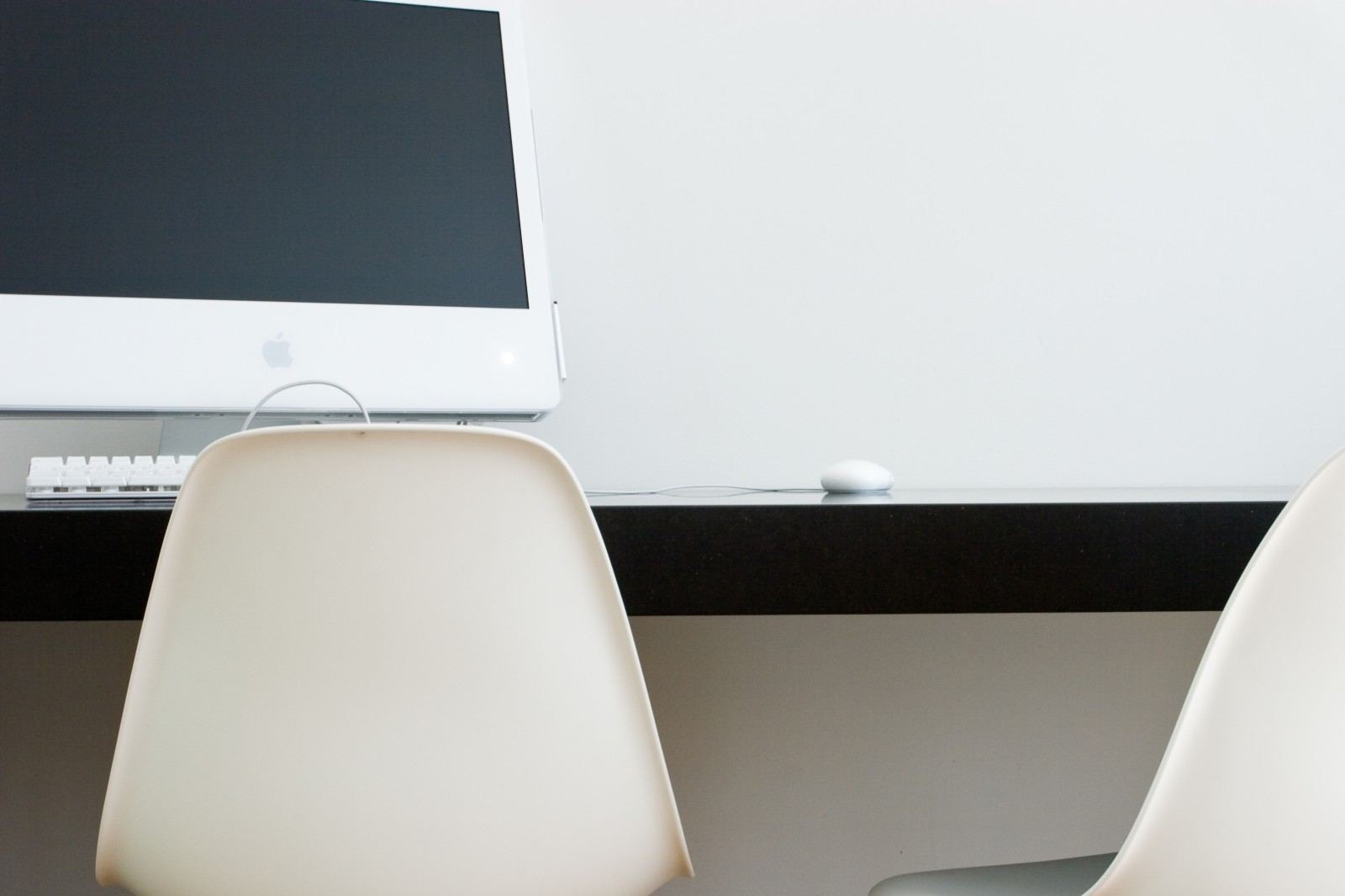 Werkplek met een strak zwart bureaublad, een computerscherm en witte kuipstoelen ervoor.