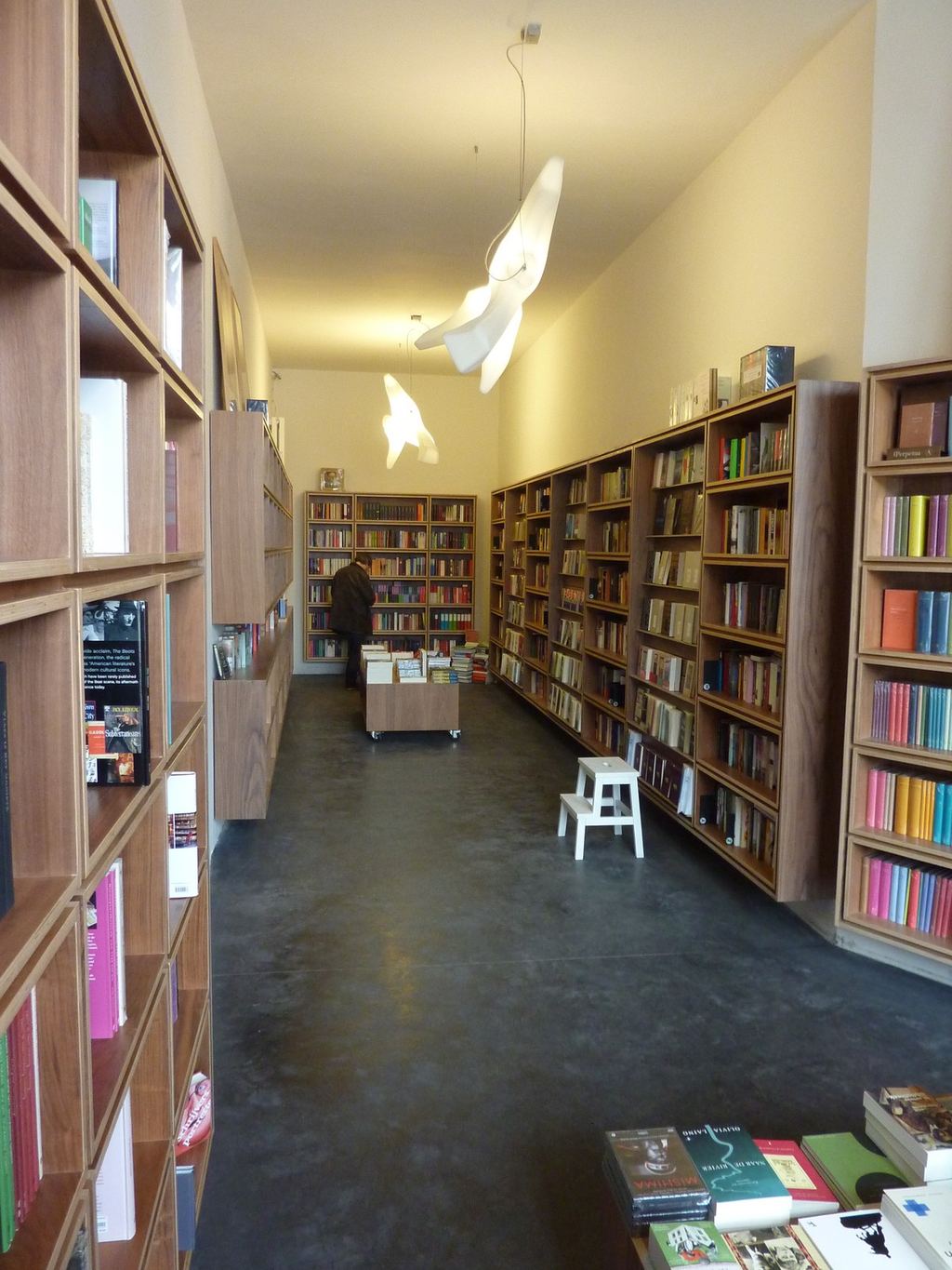 Wandvullende boekenkast van licht hout, opgebouwd uit vierkante vakken tot aan het plafond.