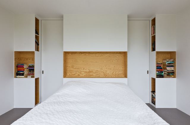 Bed met een nis van grenen multiplex en boekenkastjes aan weerszijden.