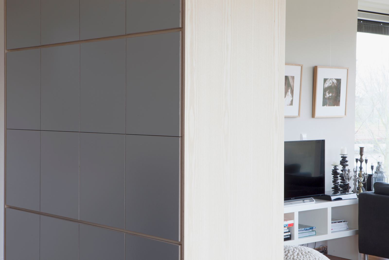 Kast met grijze fronten aan één kant en een lichte houten hoekpaal aan de andere kant.