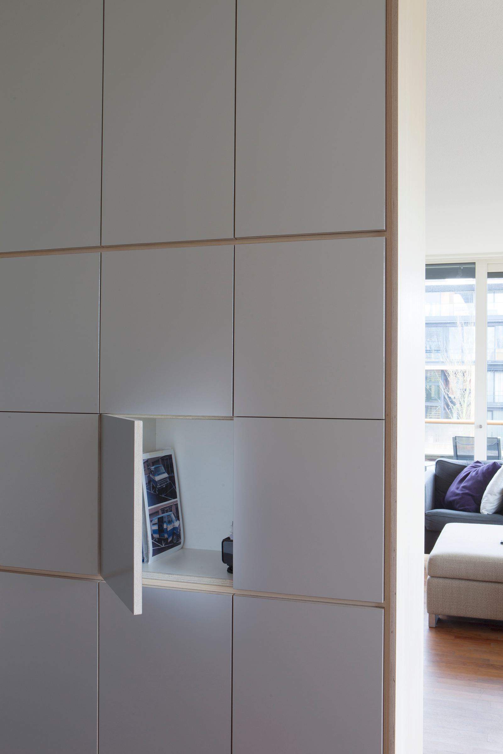 Detail van een grijze kastdeur die openstaat, met een lichte houten binnenkant.