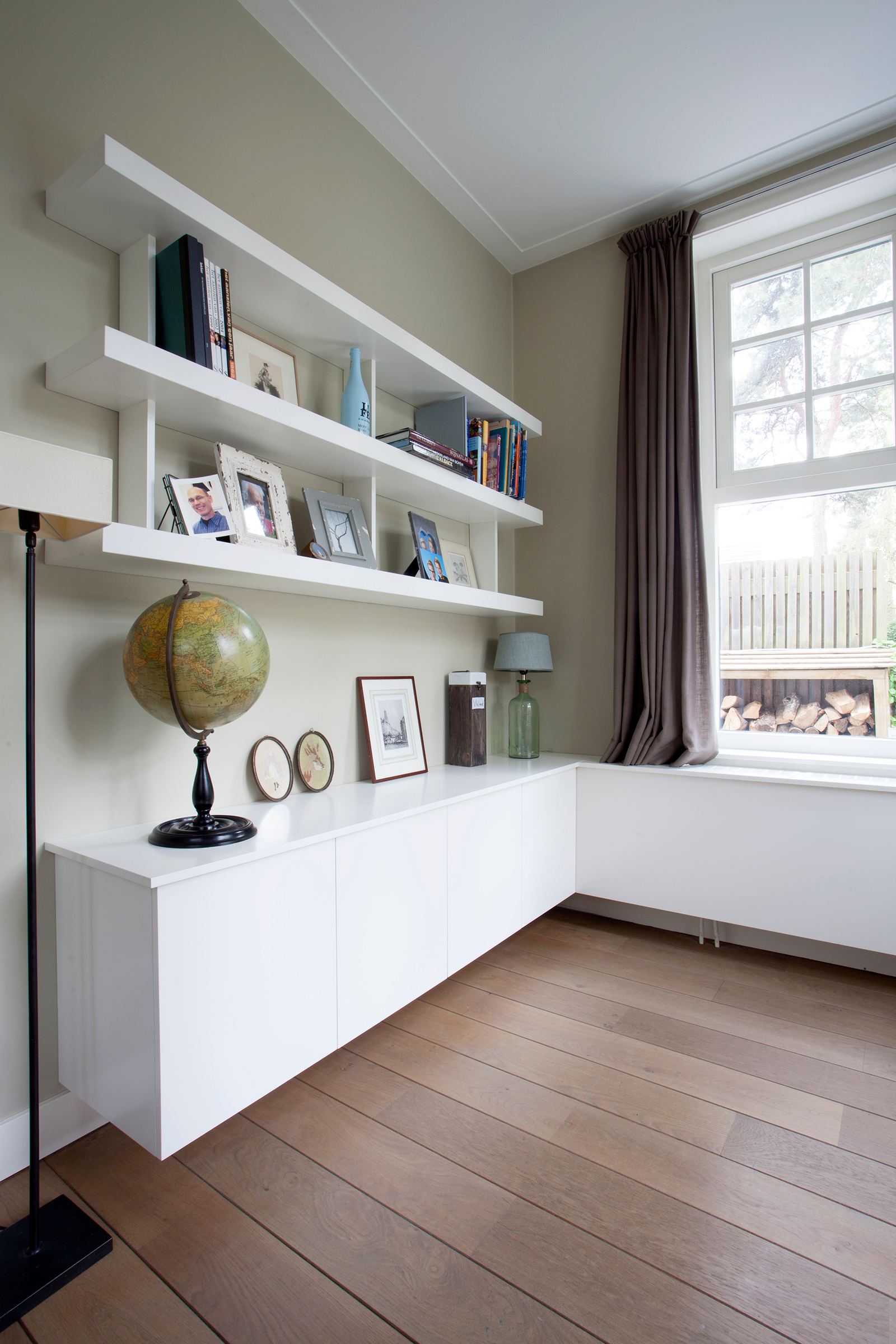 Witte zwevende planken met foto's boven een laag dressoir.