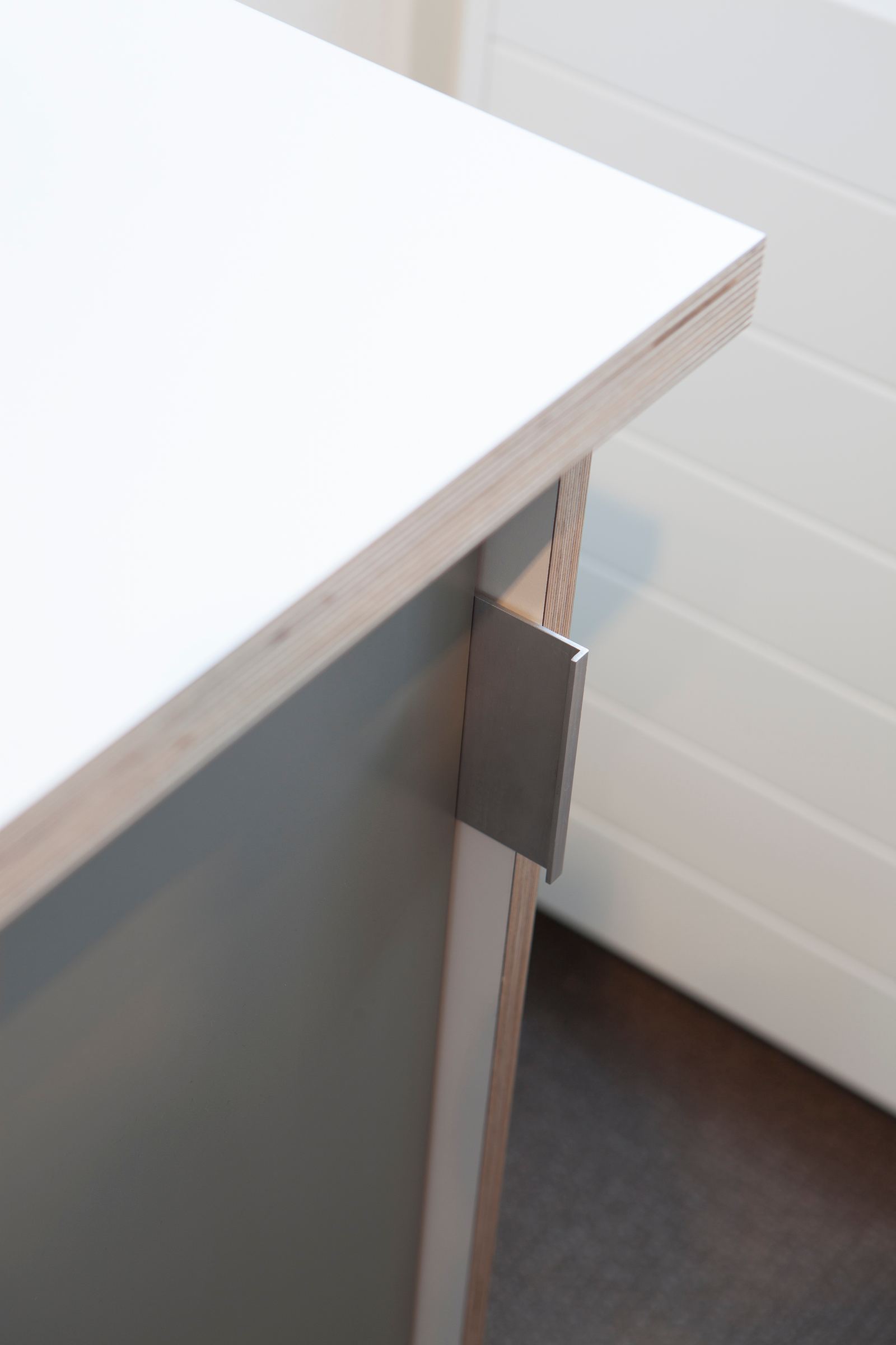 Detail van de hoek van een bureau, waar een metalen beugel het blad ondersteunt.