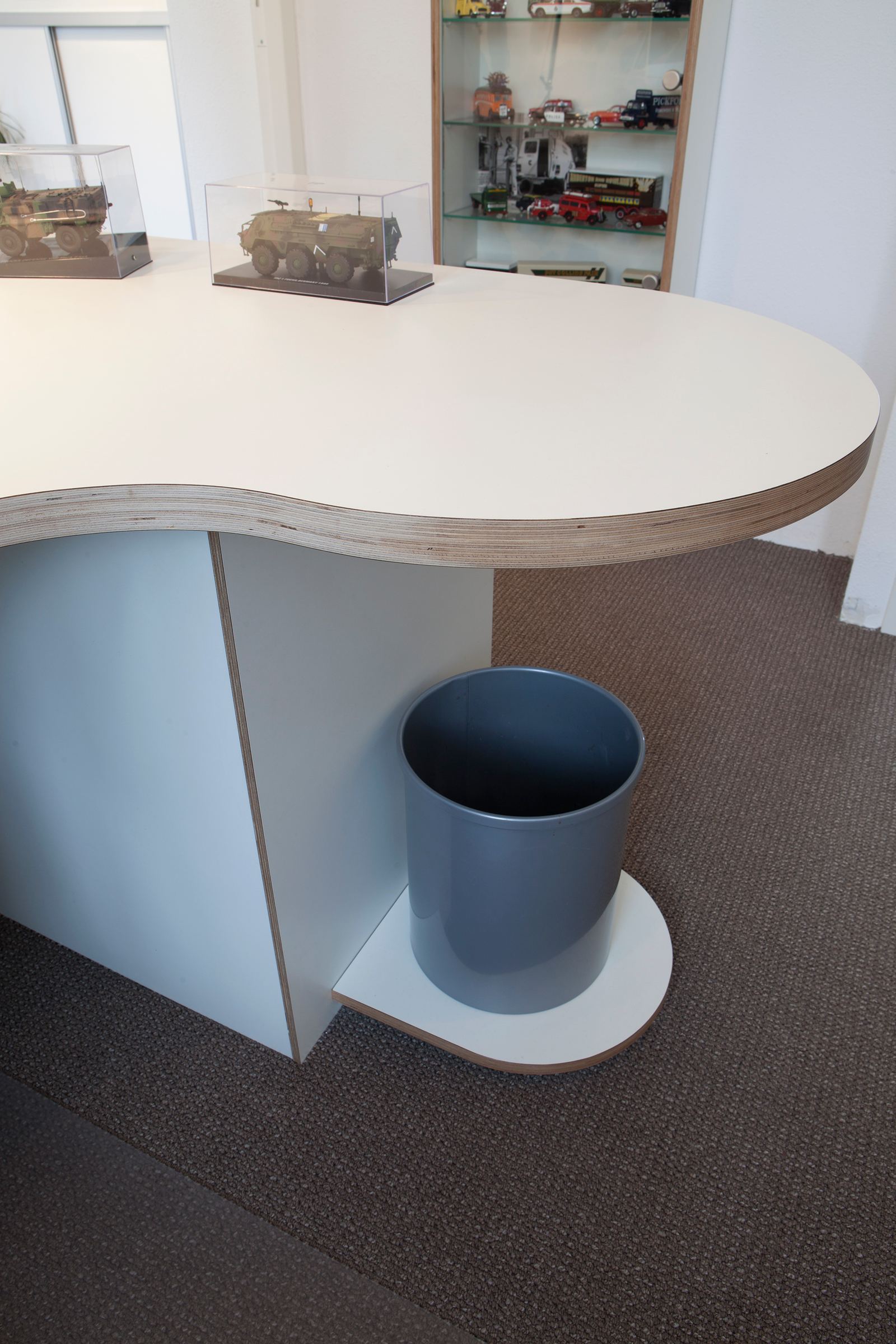 Detail van een nierkast-vormig bureaublad met plaatrand, met modelvoertuigen erop.