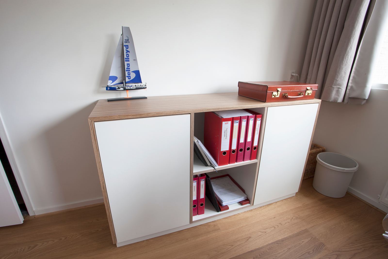Dressoir met een gestreept houten blad, witte deuren en een open middenvak met ordners.