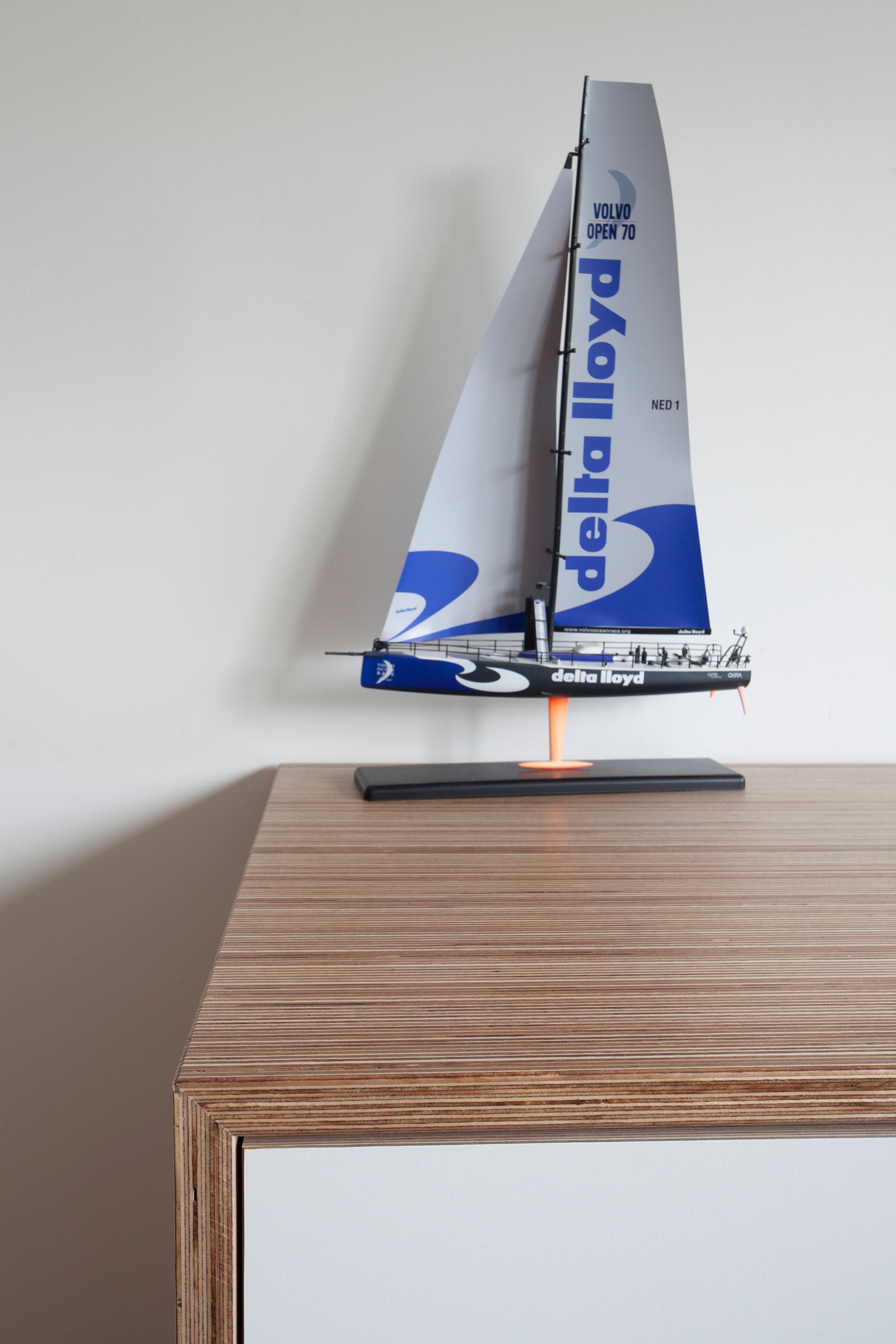 Gestreept houten blad van een dressoir, met een model zeilboot erop.